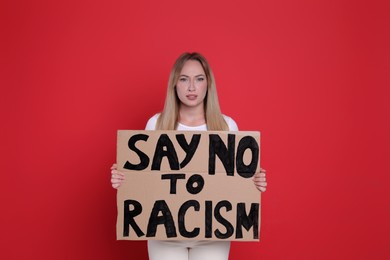 Young woman holding sign with phrase Say No To Racism on red background