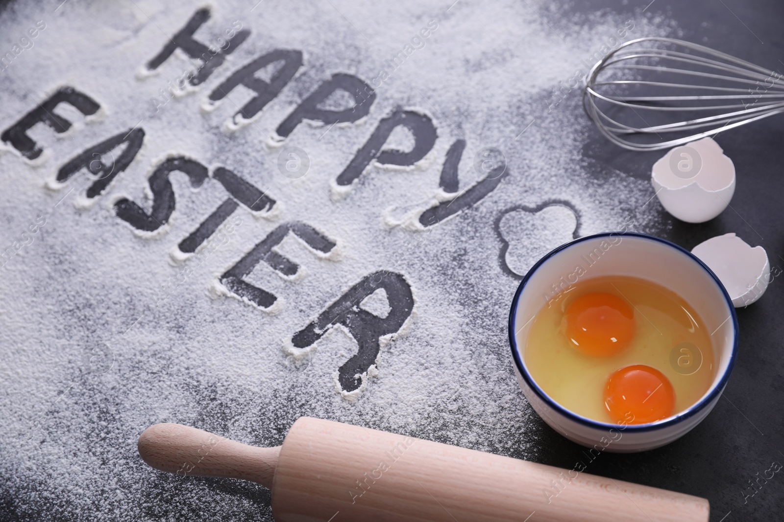 Photo of Cooking tools, eggs and words Happy Easter written in flour on black table. Baking cake
