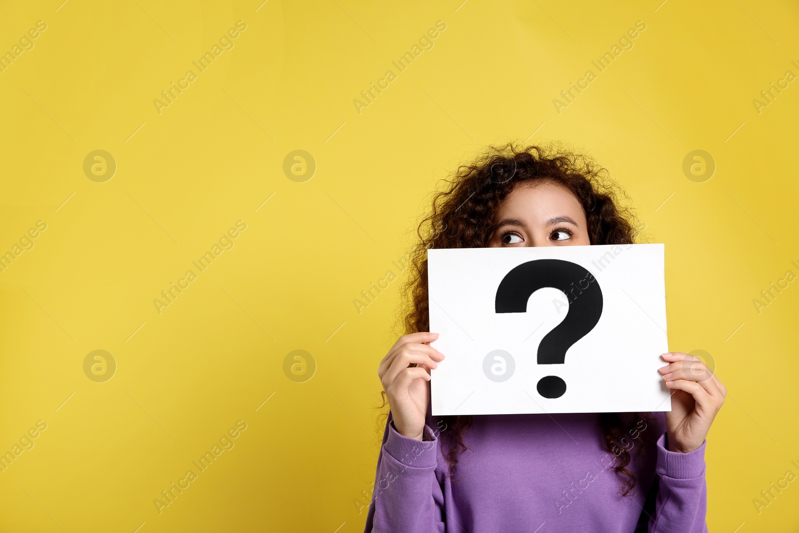 Photo of African-American woman with question mark sign on yellow background. Space for text