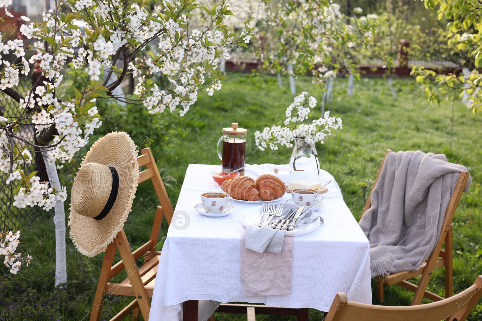 Photo of Stylish table setting with beautiful spring flowers, tea and croissants in garden