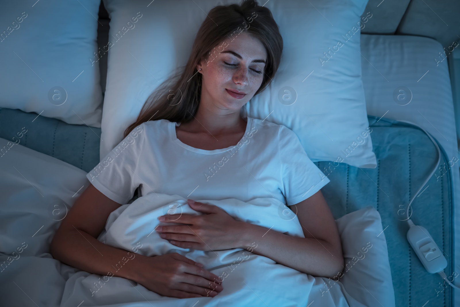 Photo of Young woman sleeping on electric heating pad in bed at night, top view