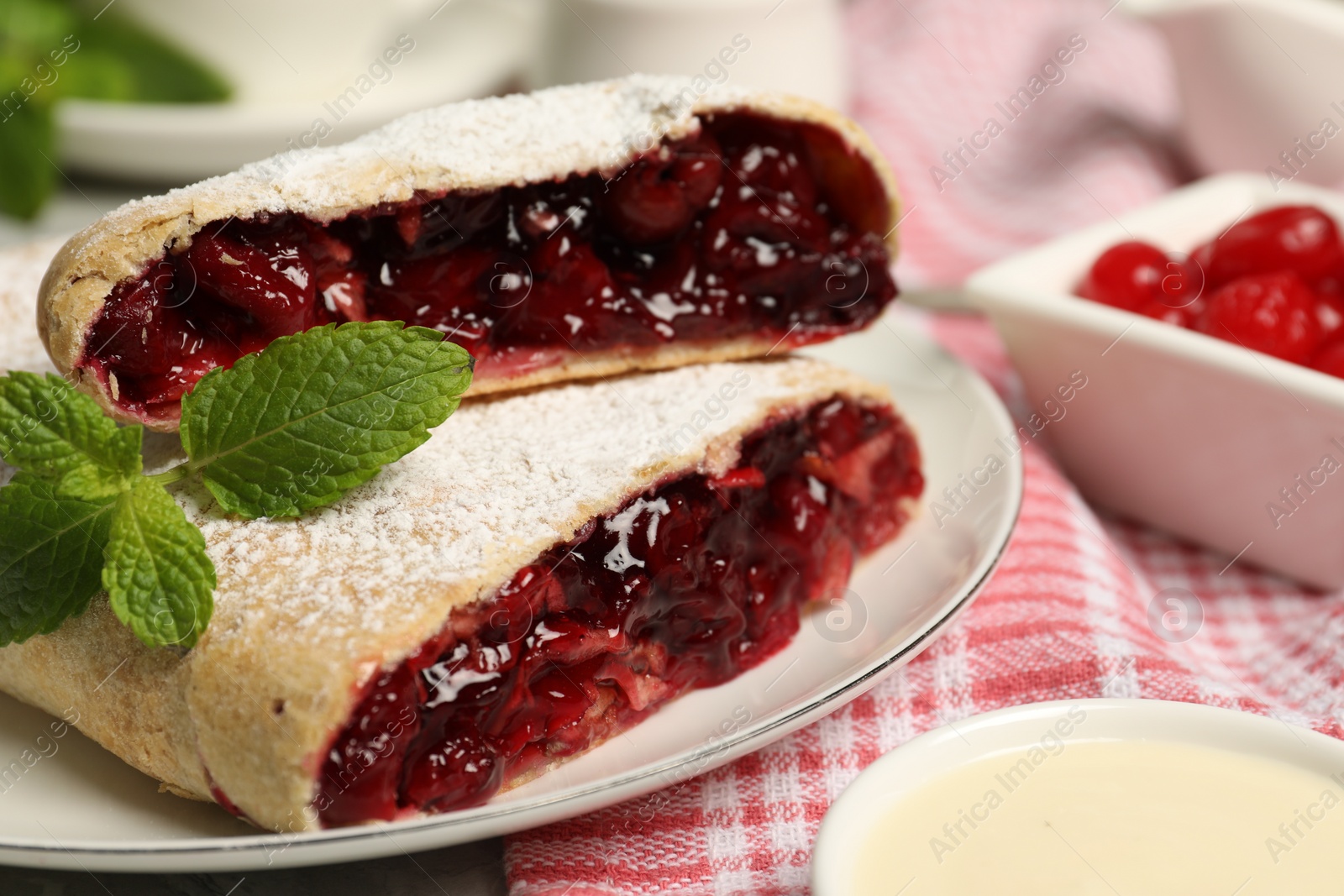 Photo of Delicious strudel with cherries, powdered sugar and mint on table, closeup