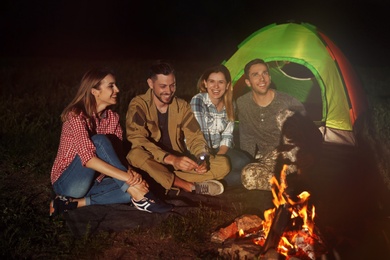 Young friends spending time near bonfire at night. Camping season