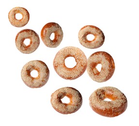 Image of Many fresh bagels with sesame seeds falling on white background