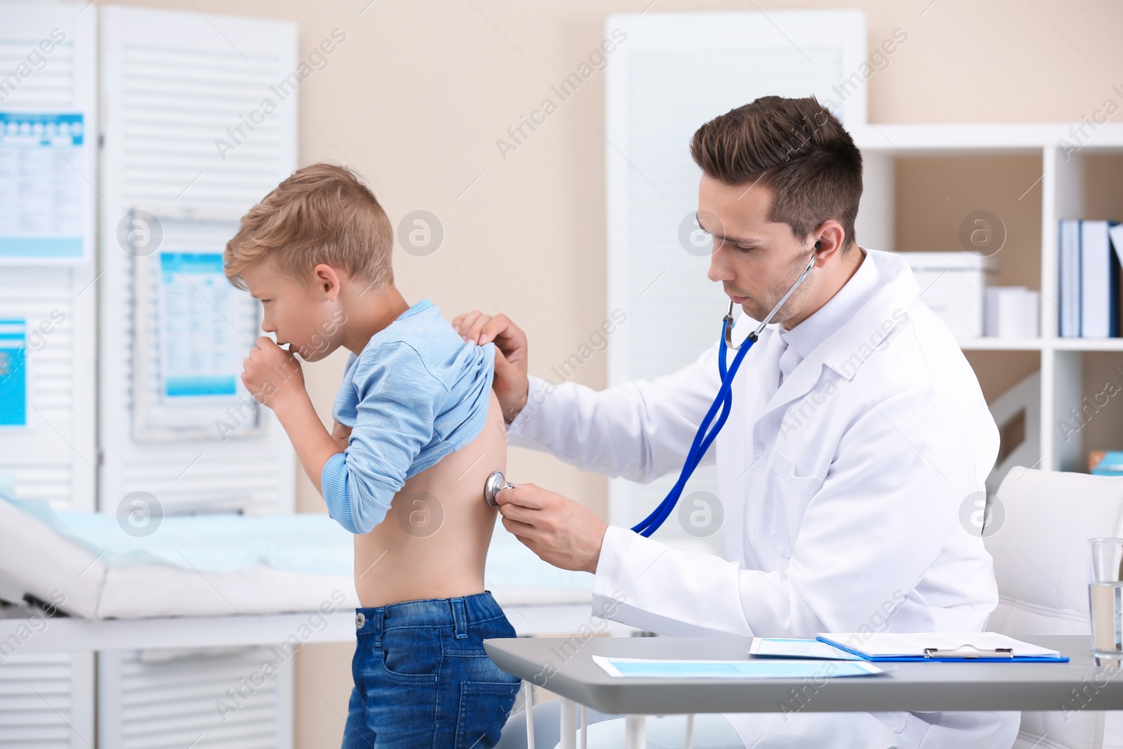 Photo of Doctor examining coughing little boy at clinic