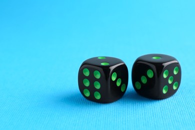 Photo of Two black game dices on light blue background, closeup