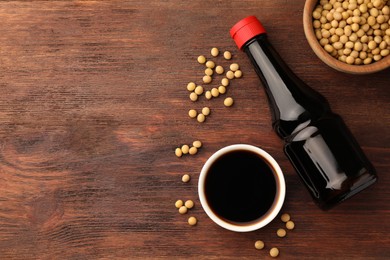 Soy sauce and soybeans on wooden table, flat lay. Space for text