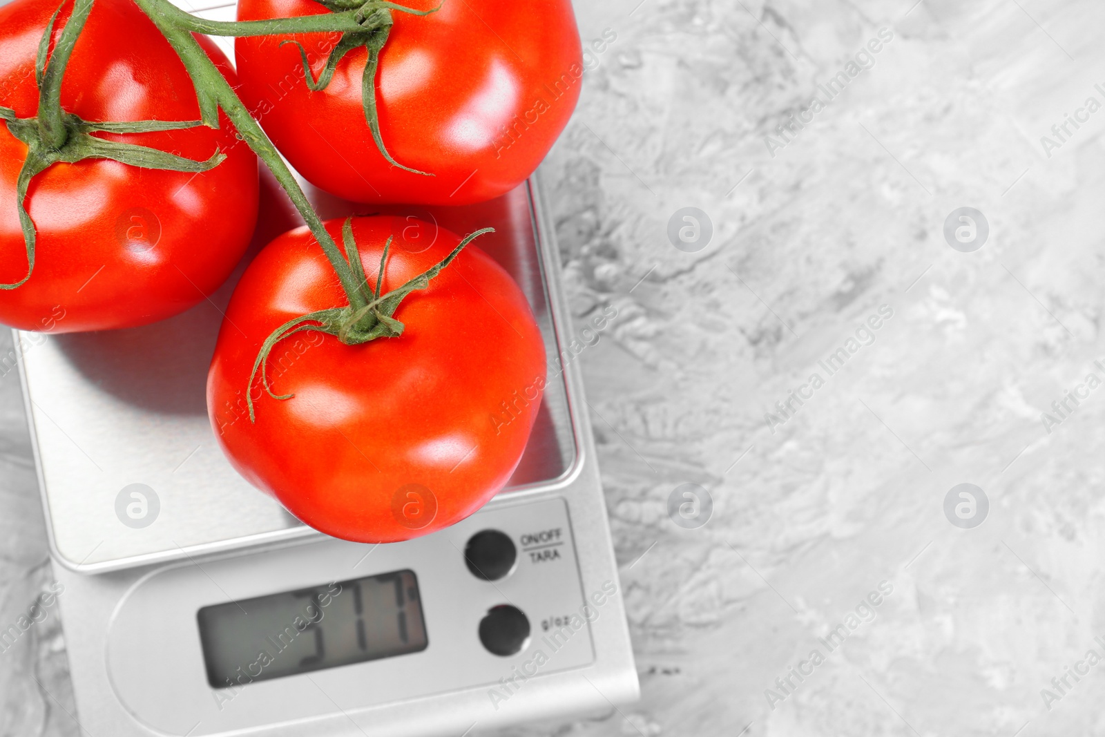 Photo of Kitchen scale with tomatoes on grey textured table, top view. Space for text