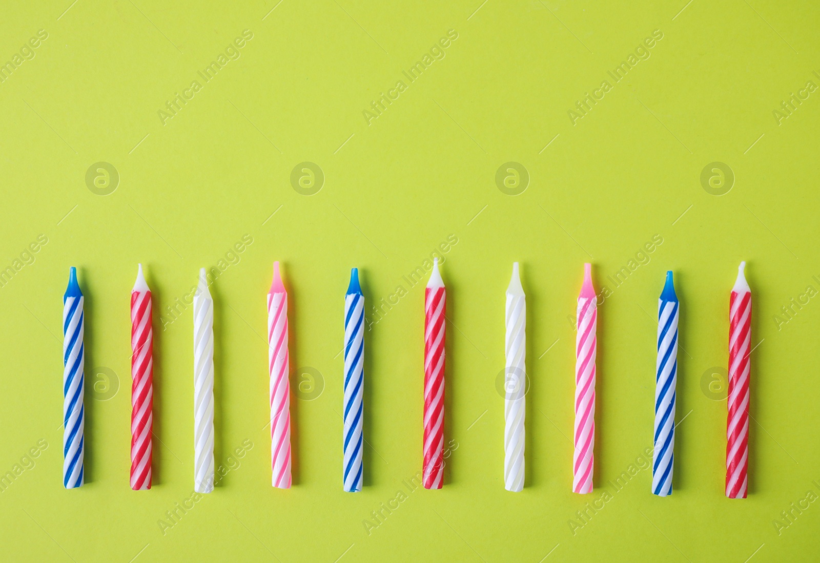 Photo of Colorful striped birthday candles on green background, top view with space for text