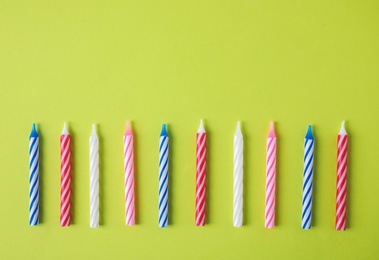 Colorful striped birthday candles on green background, top view with space for text