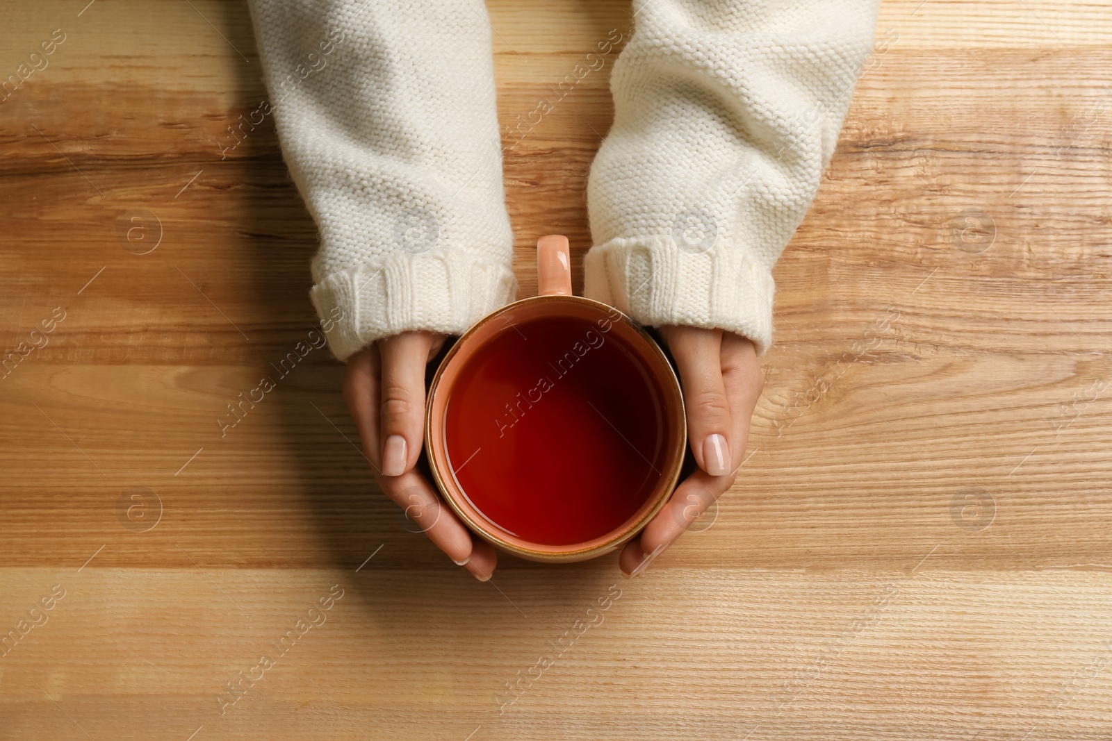 Photo of Woman holding cup of tea at wooden table, top view