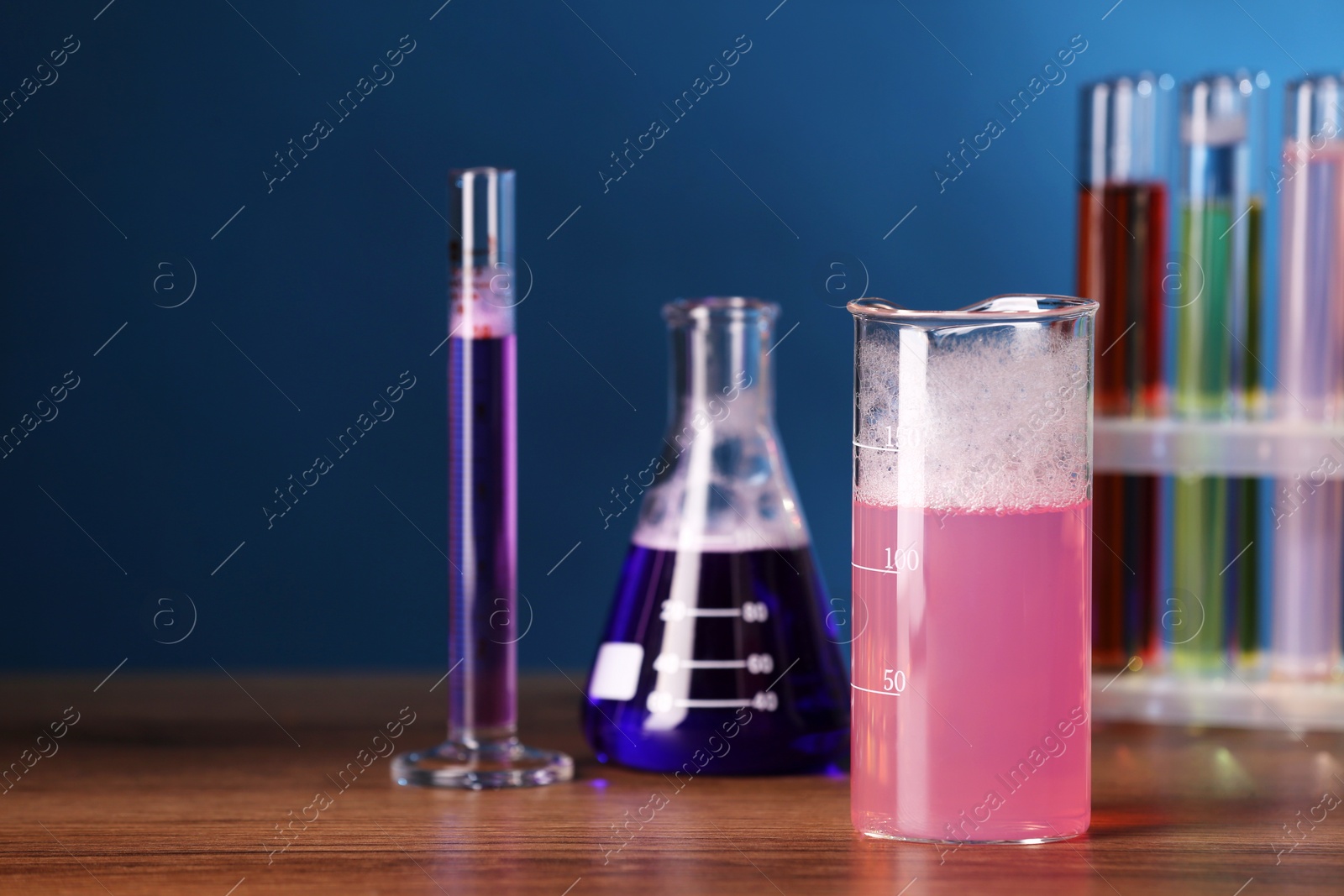 Photo of Laboratory glassware with colorful liquids on wooden table, space for text. Chemical reaction