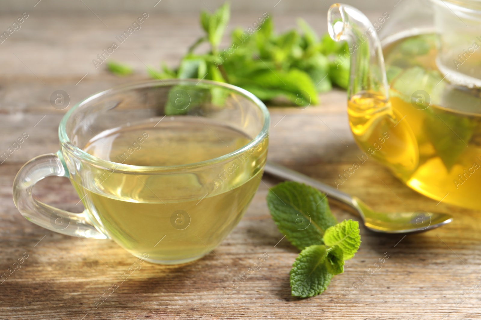 Photo of Cup and teapot with hot aromatic mint tea on wooden table