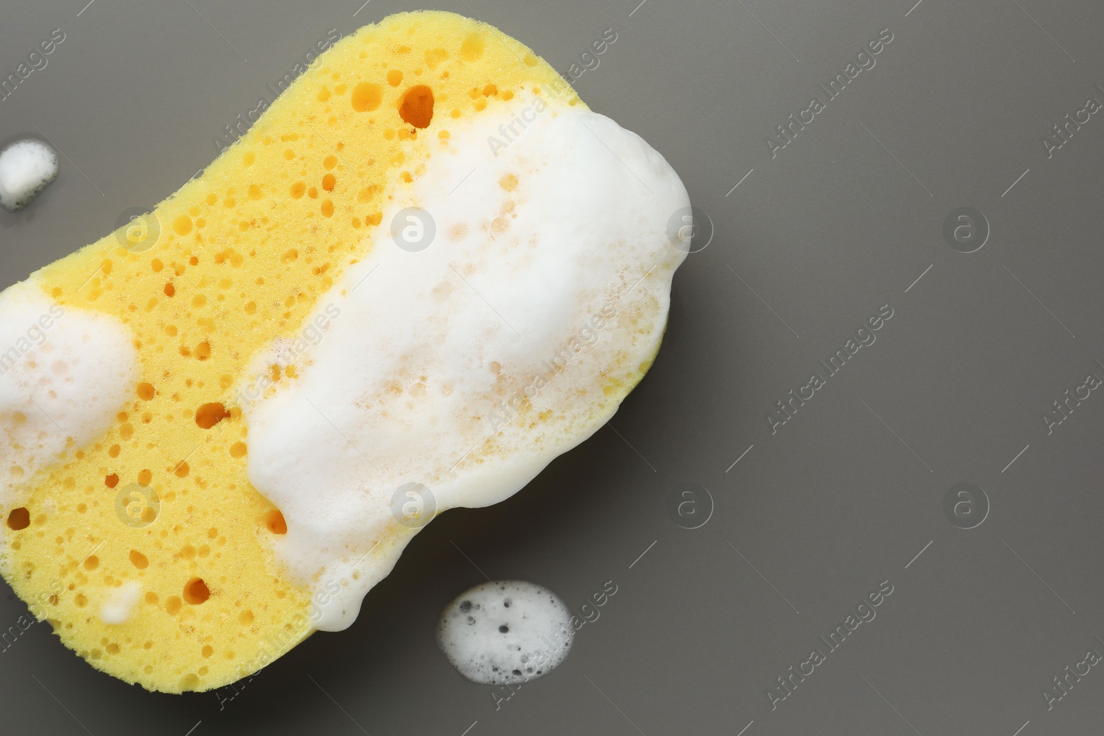 Photo of Yellow sponge with foam on grey background, top view. Space for text