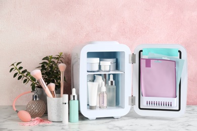 Photo of Open cosmetic refrigerator and skin care products on white marble table