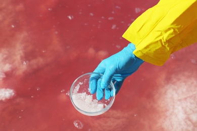 Photo of Laboratory worker with Petri dish taking sample from pink lake for analysis, closeup