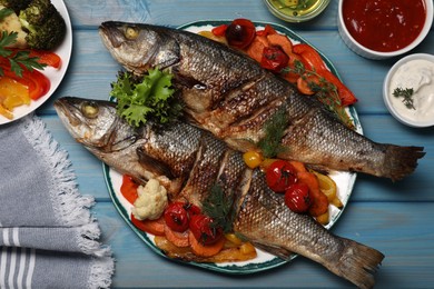 Plate with delicious baked sea bass fish and vegetables on light blue table, flat lay