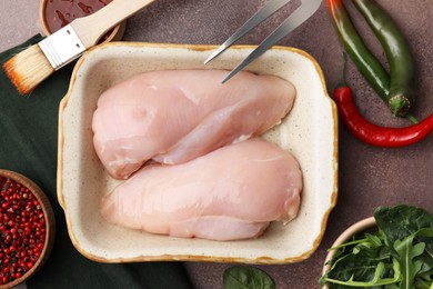 Marinade, basting brush, raw chicken and spices on brown table, flat lay