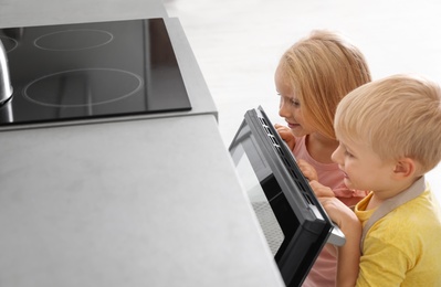 Little kids baking something in oven at home