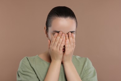 Photo of Resentful woman covering face with hands on brown background