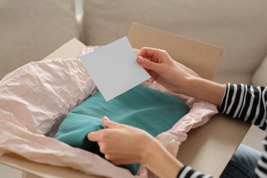 Woman holding greeting card near parcel with Christmas gift indoors, closeup