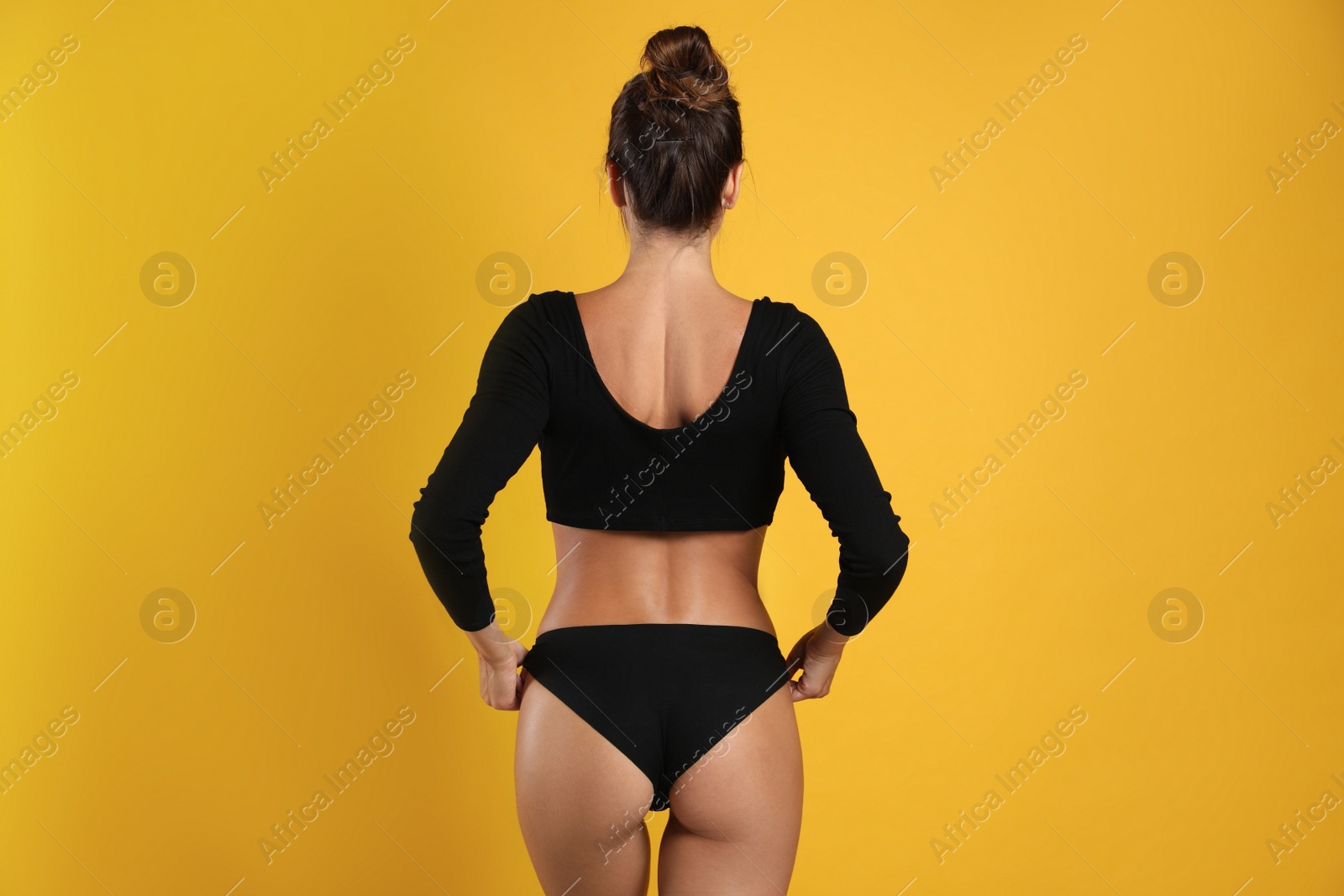 Photo of Woman in black sexy panties on yellow background, back view