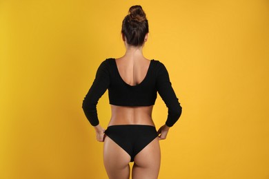 Photo of Woman in black sexy panties on yellow background, back view