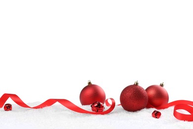 Beautiful red Christmas balls, ribbon and sleigh bells on snow against white background