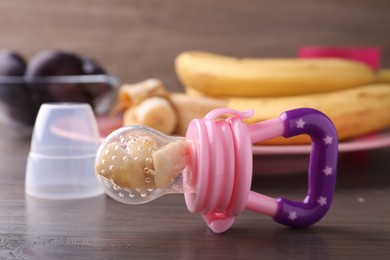 Photo of Nibbler with fresh banana on wooden table. Baby feeder