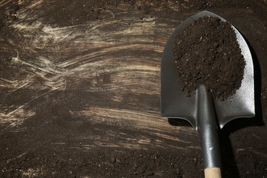 Photo of Metal shovel with fertile soil on dirty wooden surface, top view. Space for text