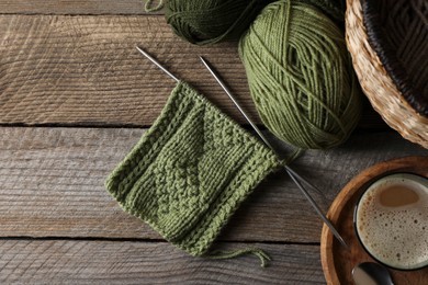 Soft green woolen yarn, knitting, needles and glass of drink on wooden table, flat lay. Space for text