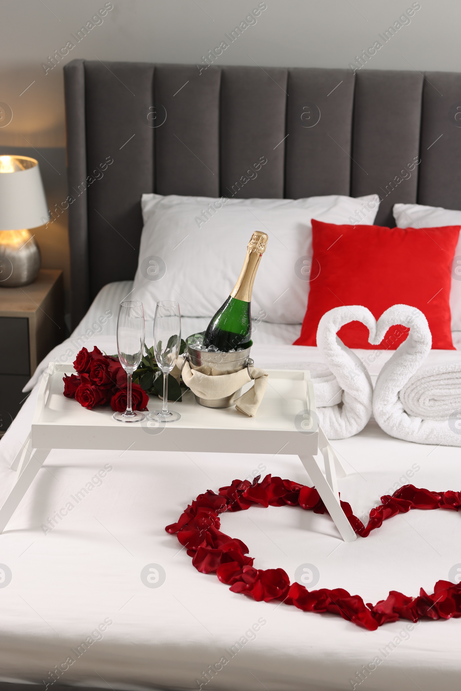 Photo of Honeymoon. Swans made with towels, heart of beautiful rose petals and sparkling wine on bed in room