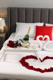 Honeymoon. Swans made with towels, heart of beautiful rose petals and sparkling wine on bed in room