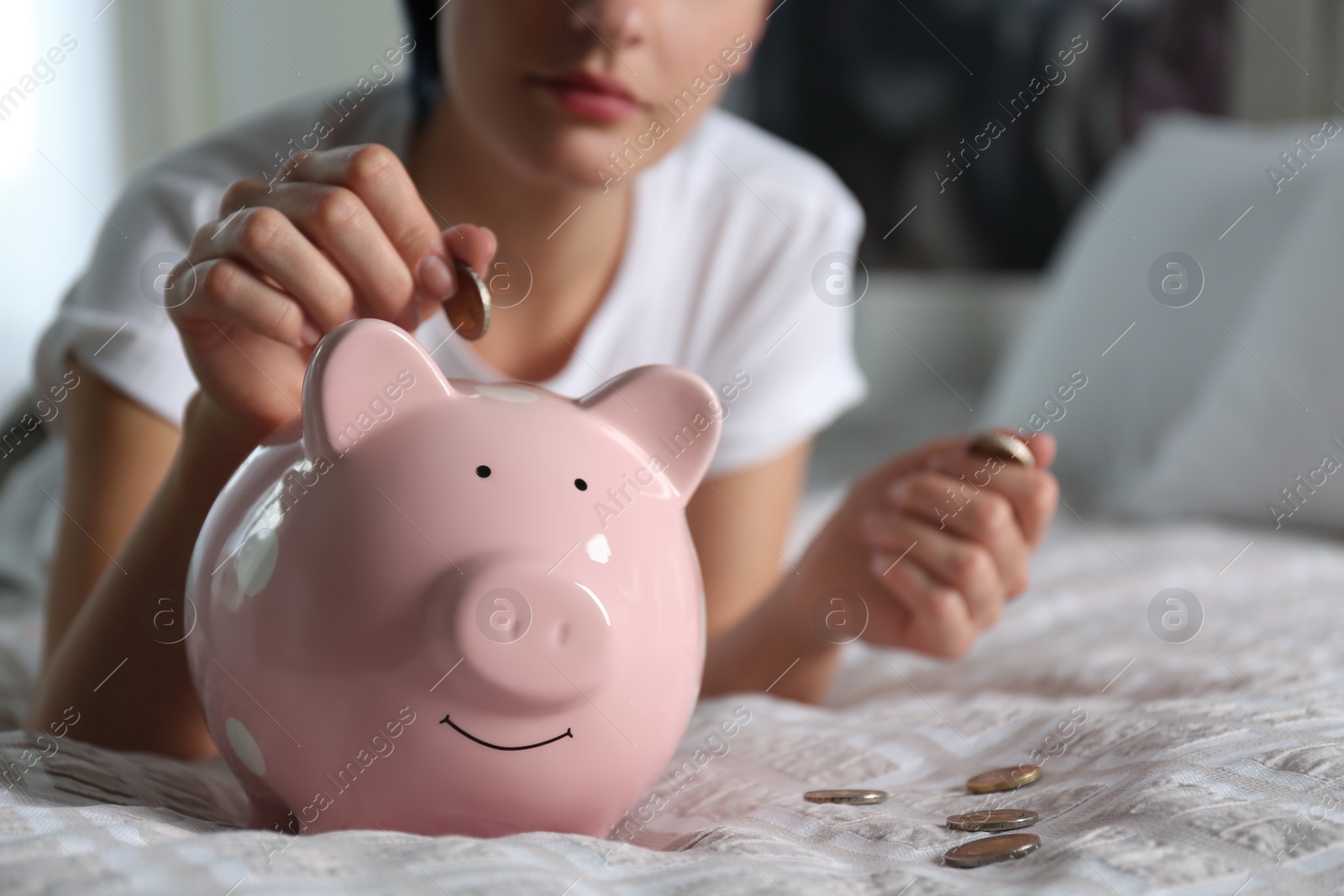 Photo of Woman putting money into piggy bank on bed at home, closeup