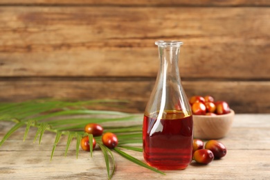 Palm oil in glass bottle, tropical leaf and fruits on wooden table. Space for text