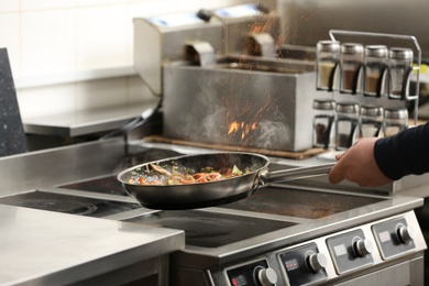 Photo of Male chef cooking tasty food on stove in restaurant 
kitchen, closeup of hand
