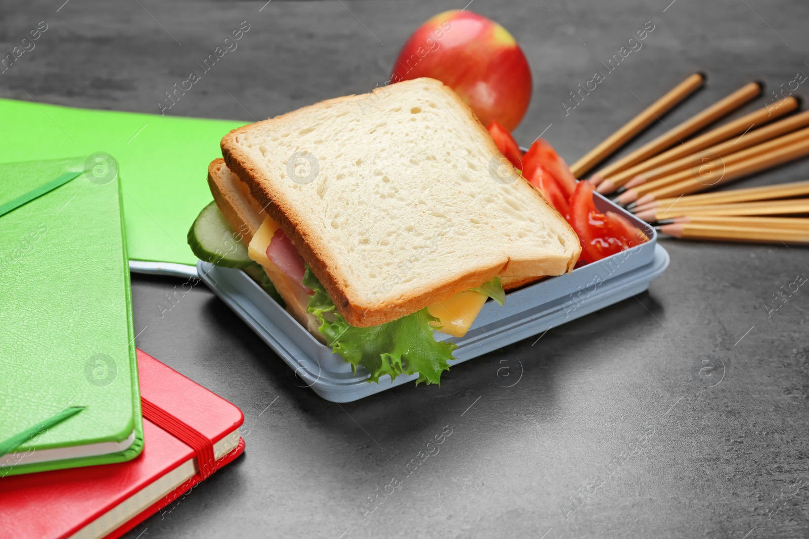 Photo of Lunch box with tasty sandwich and stationery on table