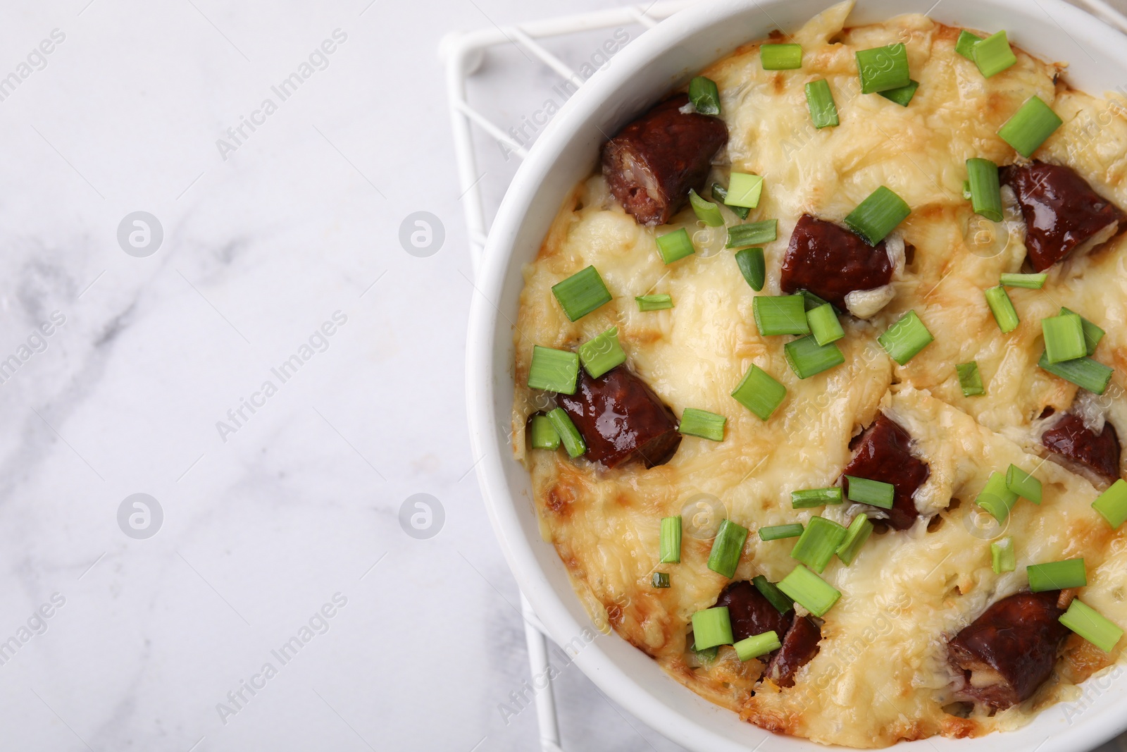 Photo of Tasty sausage casserole in baking dish on white marble table, top view. Space for text