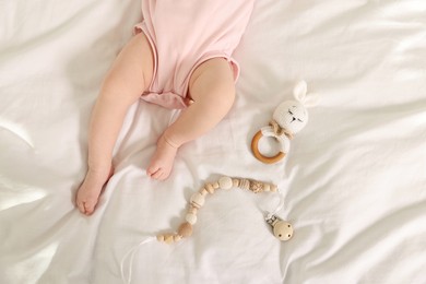 Photo of Cute baby with rattle and teether toys on sheets, top view