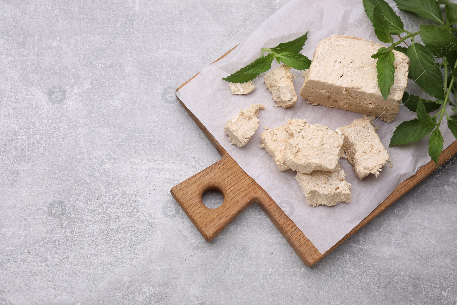 Photo of Pieces of tasty halva and mint leaves on light grey table, top view. Space for text