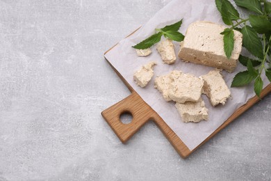 Pieces of tasty halva and mint leaves on light grey table, top view. Space for text