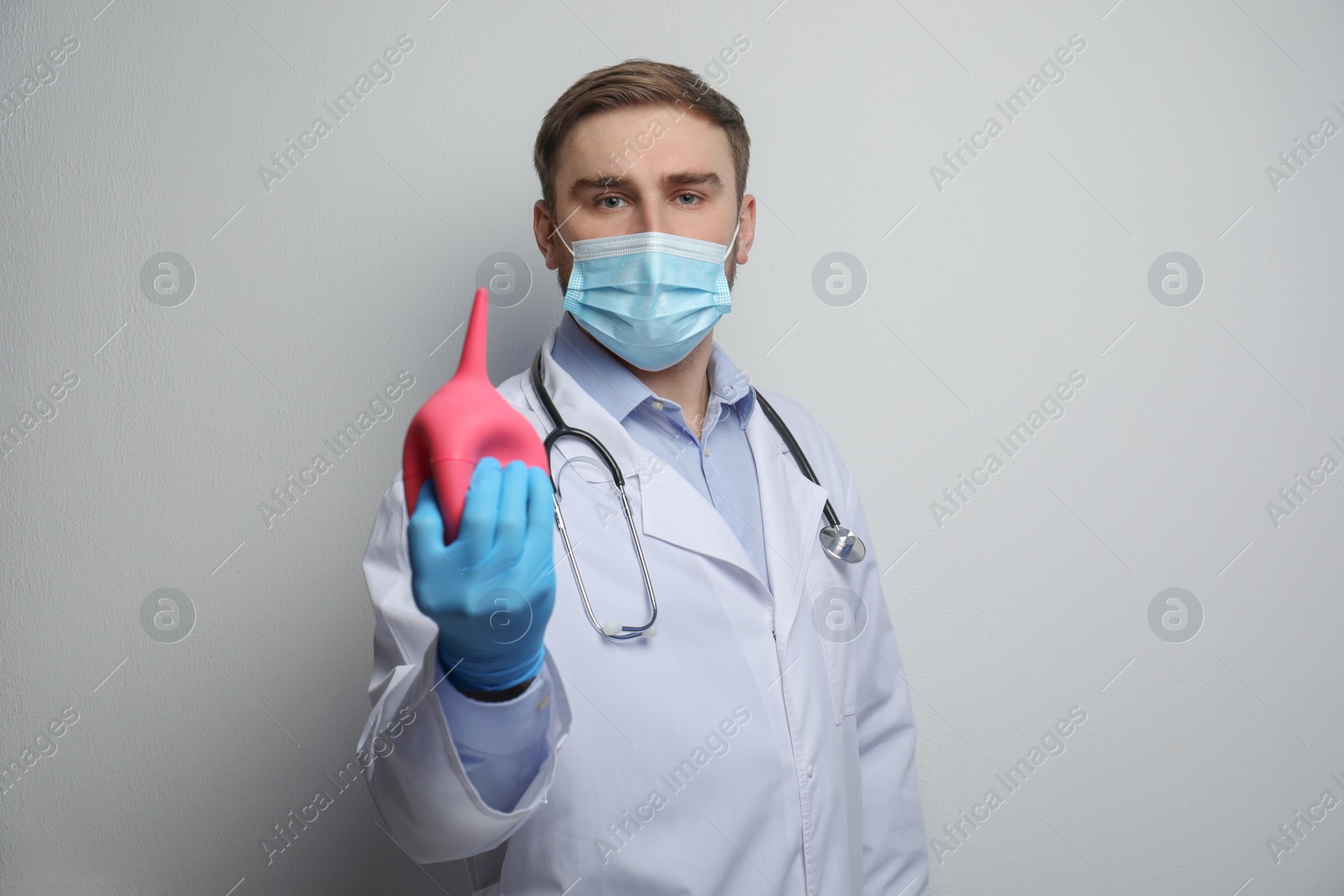 Photo of Doctor holding rubber enema on grey background