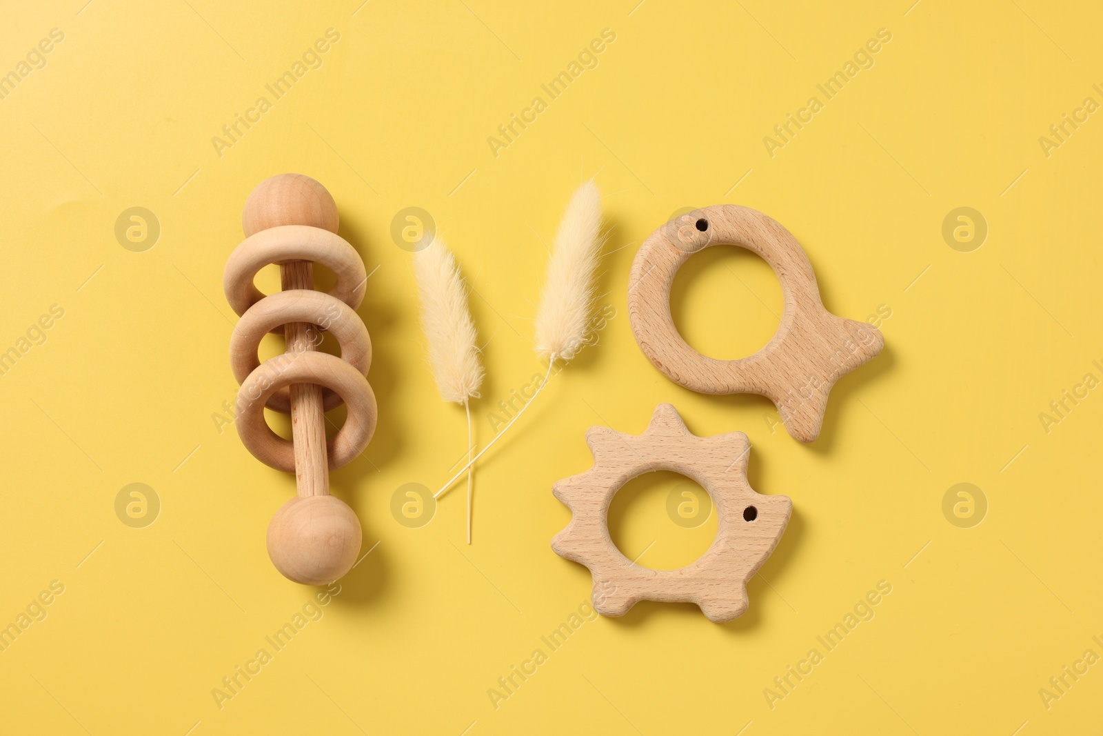 Photo of Baby accessories. Wooden rattle, teethers and dry spikes on yellow background, flat lay