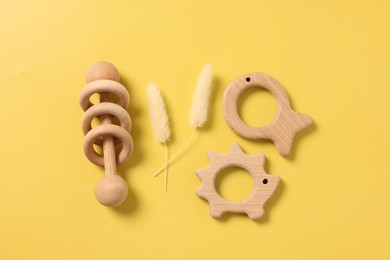Baby accessories. Wooden rattle, teethers and dry spikes on yellow background, flat lay