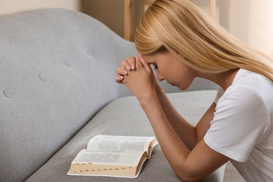 Photo of Religious young woman with Bible praying indoors