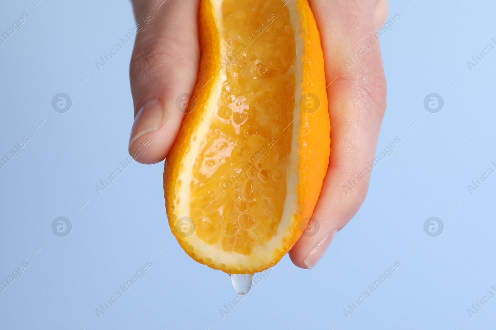 Photo of Woman squeezing juicy orange on light blue background, closeup