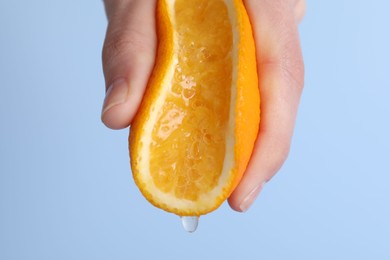Photo of Woman squeezing juicy orange on light blue background, closeup