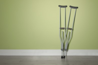 Photo of Pair of axillary crutches near light green wall. Space for text