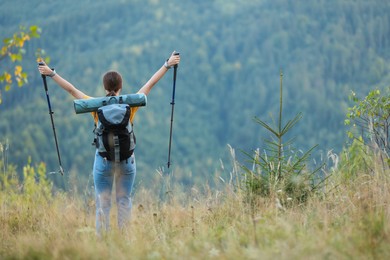 Photo of Woman with backpack and trekking poles hiking in mountains, back view. Space for text