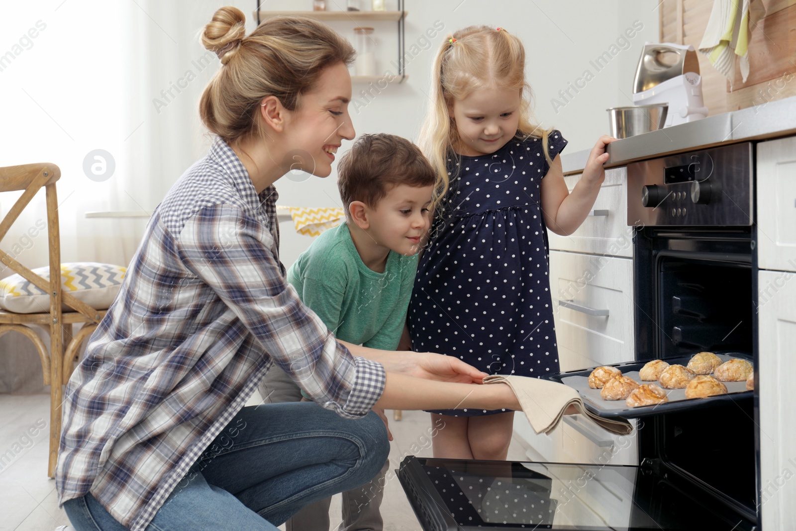 Photo of Mother and her children taking out cookies from oven in kitchen